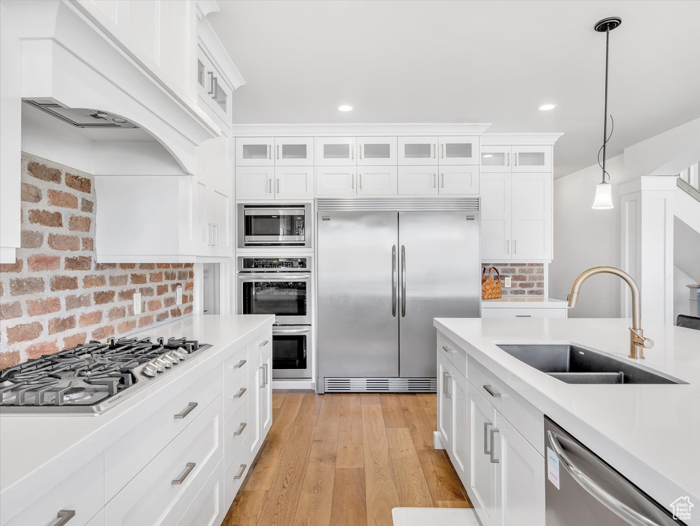 Kitchen with built in appliances, a sink, light countertops, hanging light fixtures, and white cabinets