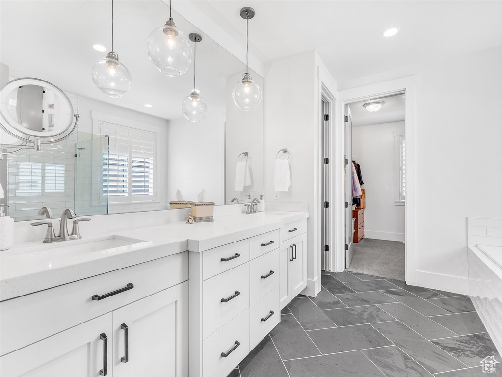 Bathroom featuring a shower stall, double vanity, a tub, and baseboards