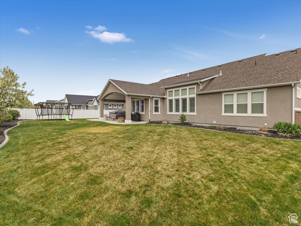 Rear view of house with a trampoline, a patio, stucco siding, and roof with shingles