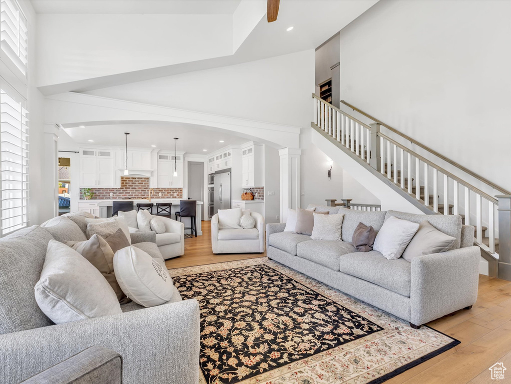 Living room featuring a high ceiling, light wood-style floors, arched walkways, recessed lighting, and stairway
