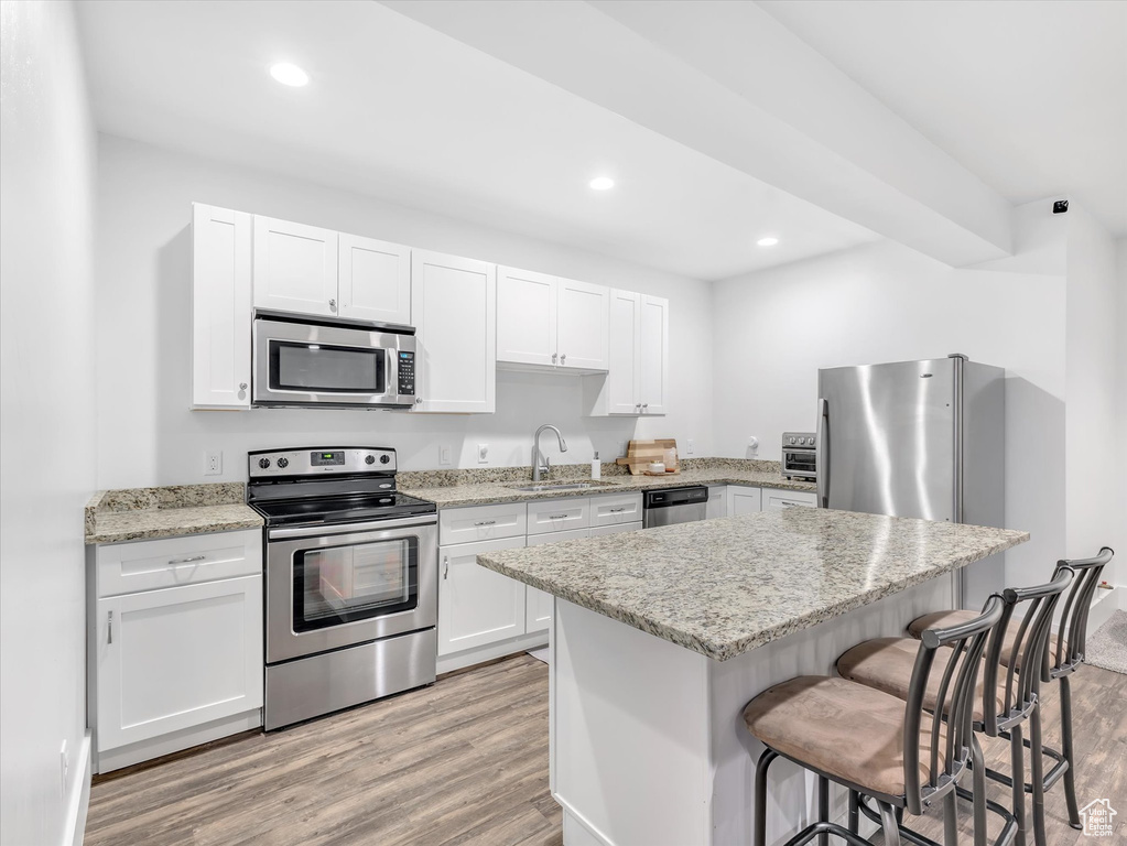 Kitchen featuring appliances with stainless steel finishes, a sink, light wood finished floors, a breakfast bar, and recessed lighting