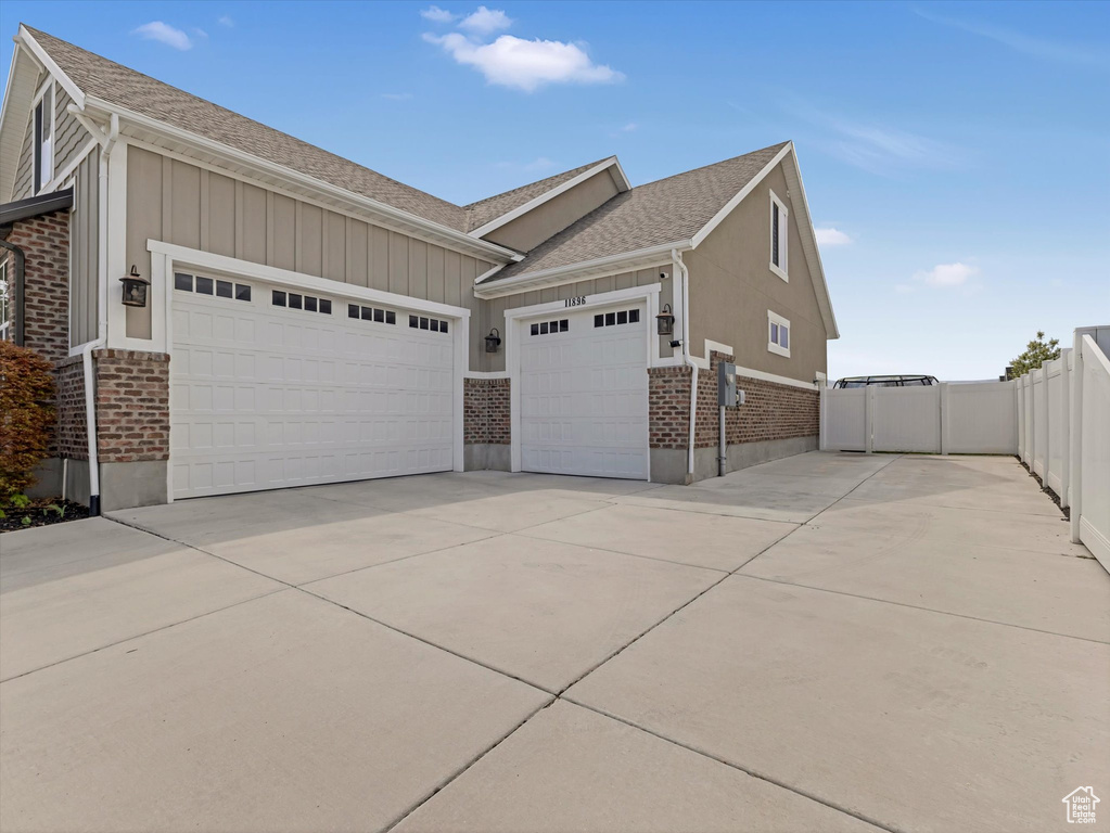 View of property exterior with brick siding, a garage, driveway, board and batten siding, and a shingled roof