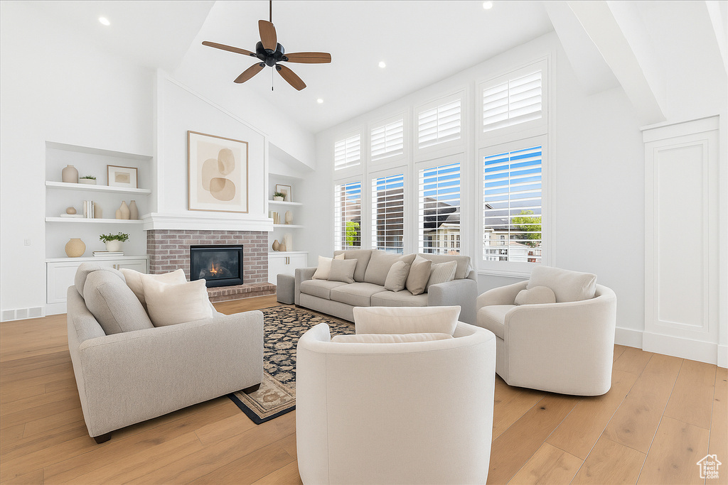 Living room with high vaulted ceiling, ceiling fan, light wood-style flooring, built in features, and a brick fireplace