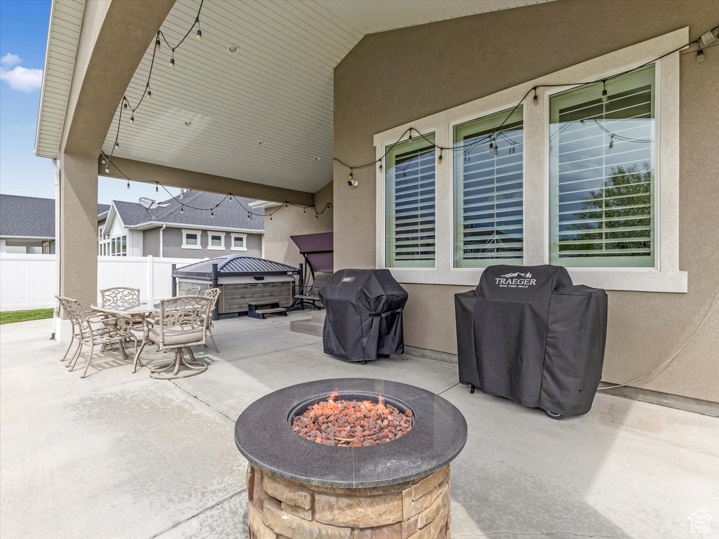 View of patio / terrace with an outdoor fire pit, fence, outdoor dining area, a hot tub, and a grill