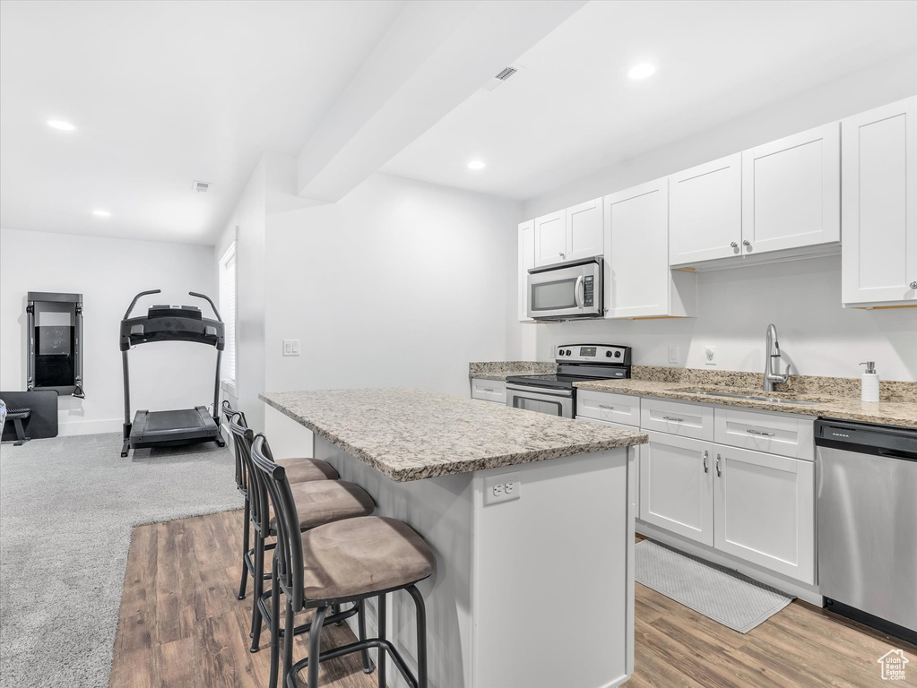 Kitchen featuring stainless steel appliances, a sink, a kitchen island, a breakfast bar area, and white cabinetry