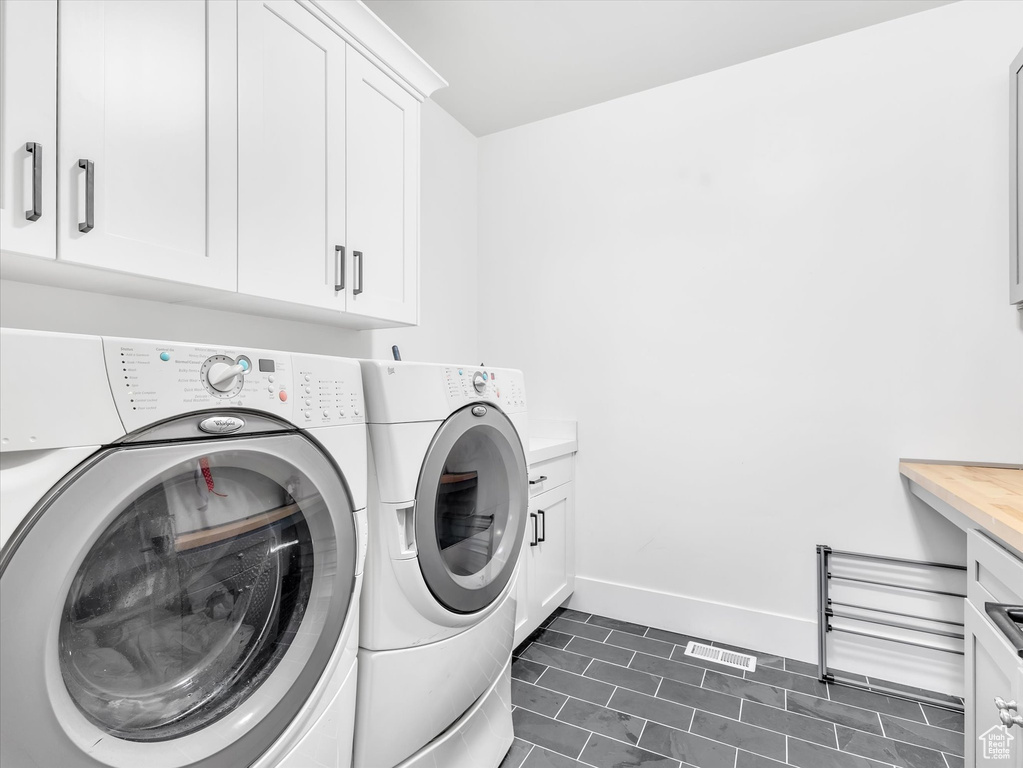Laundry room featuring washing machine and clothes dryer, cabinet space, baseboards, and dark tile patterned flooring