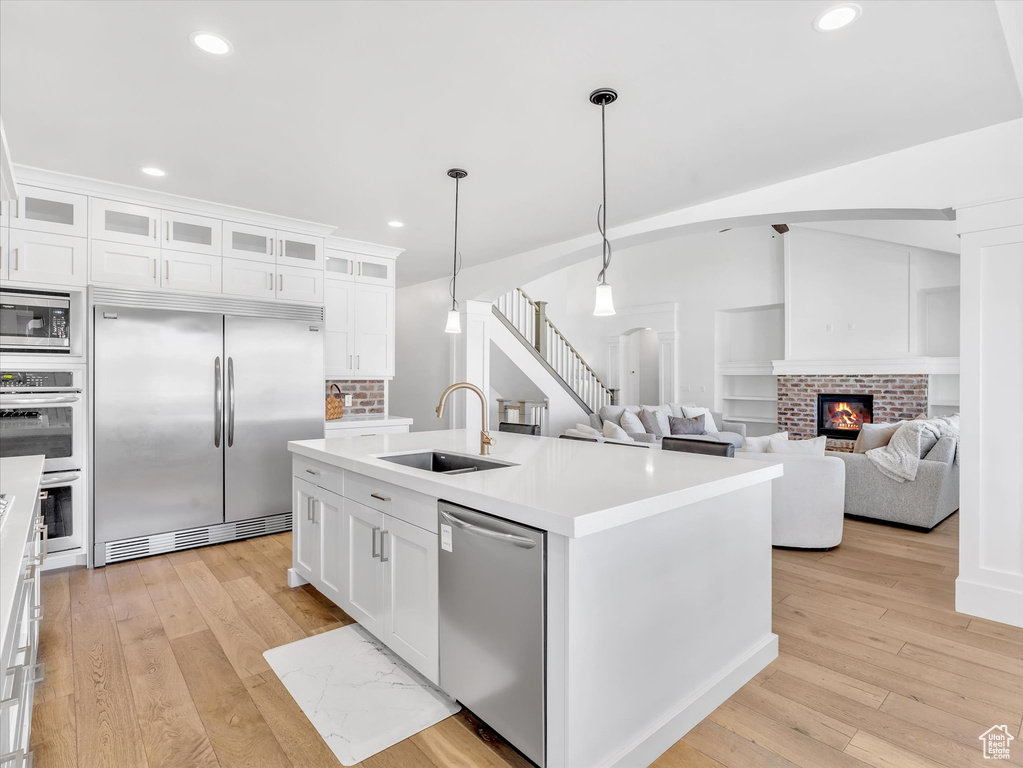 Kitchen with built in appliances, a sink, a brick fireplace, light wood-type flooring, and light countertops