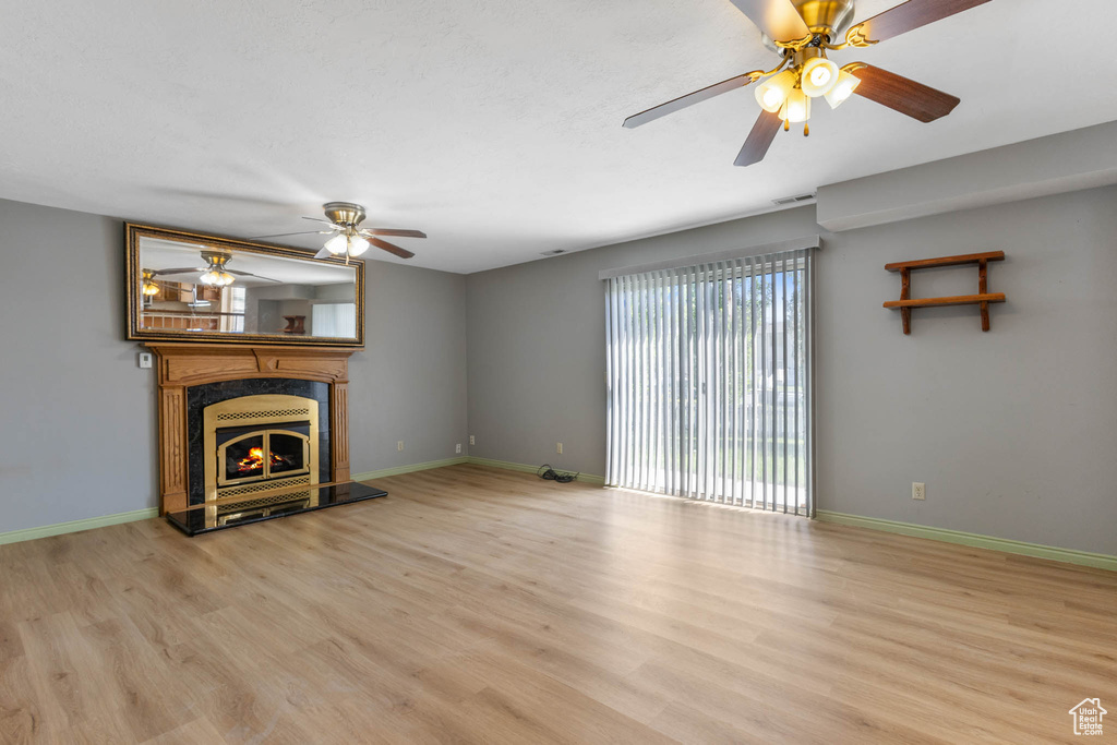 Unfurnished living room with wood finished floors, a ceiling fan, and a fireplace