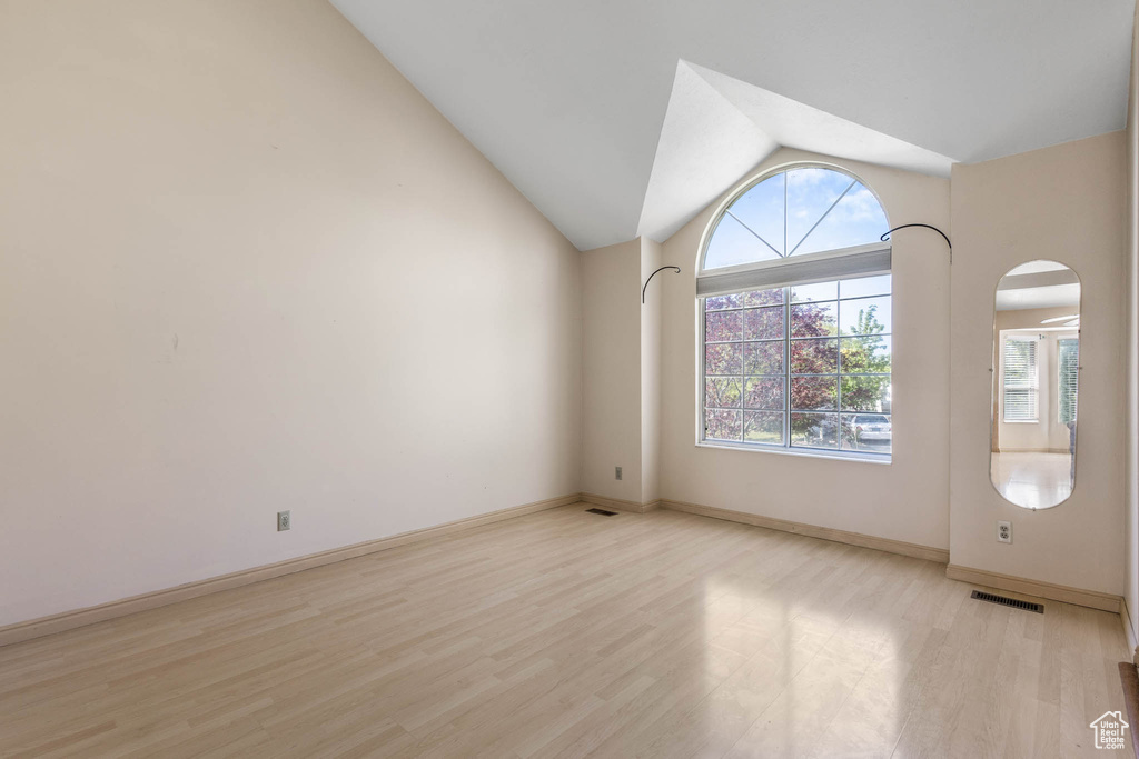 Empty room with light wood-style floors, arched walkways, lofted ceiling, and baseboards