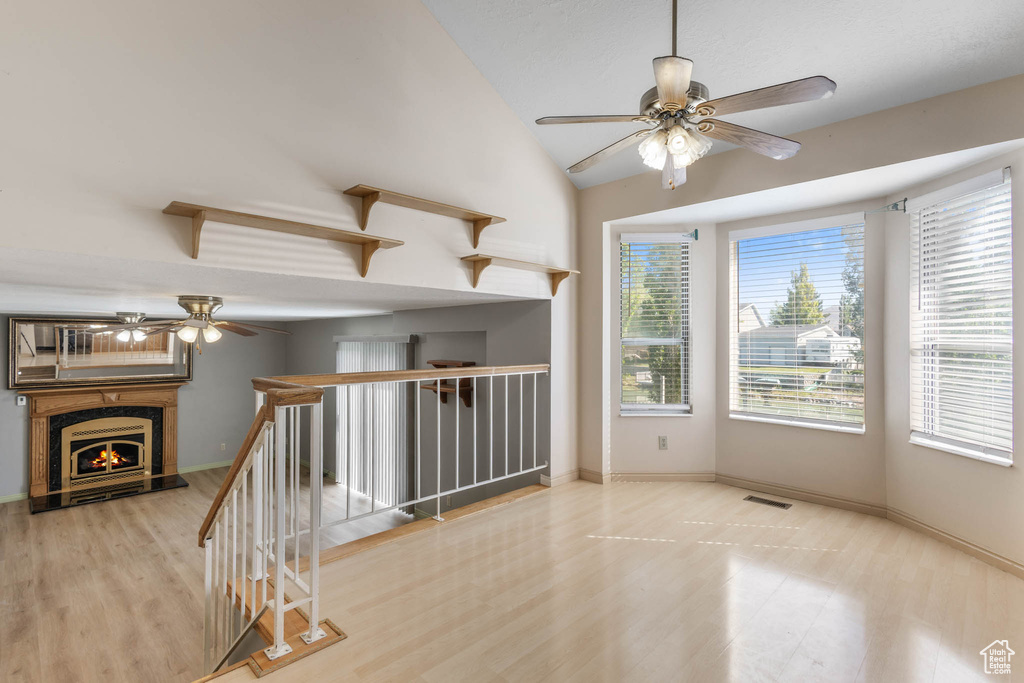 Unfurnished room with ceiling fan, wood finished floors, vaulted ceiling, a warm lit fireplace, and baseboards