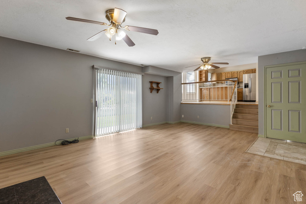 Unfurnished living room featuring a ceiling fan, light wood-style floors, stairs, and baseboards