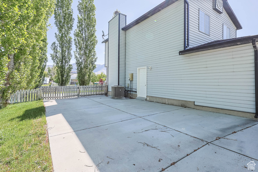 View of side of property featuring a patio area, central AC unit, a chimney, and fence