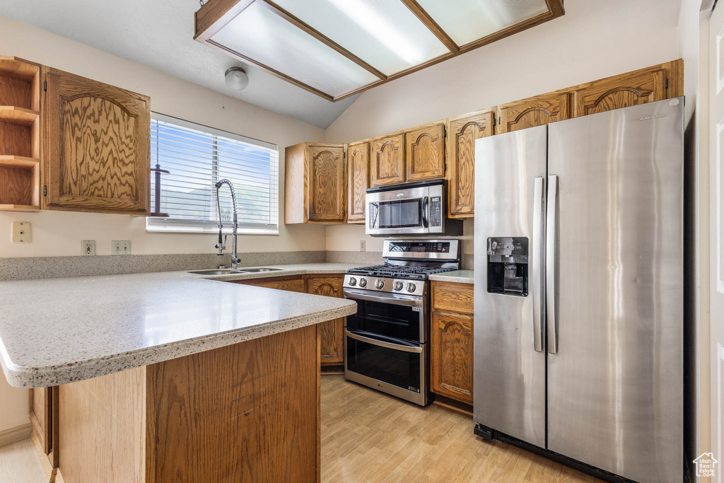 Kitchen featuring appliances with stainless steel finishes, a sink, a peninsula, light countertops, and light wood finished floors