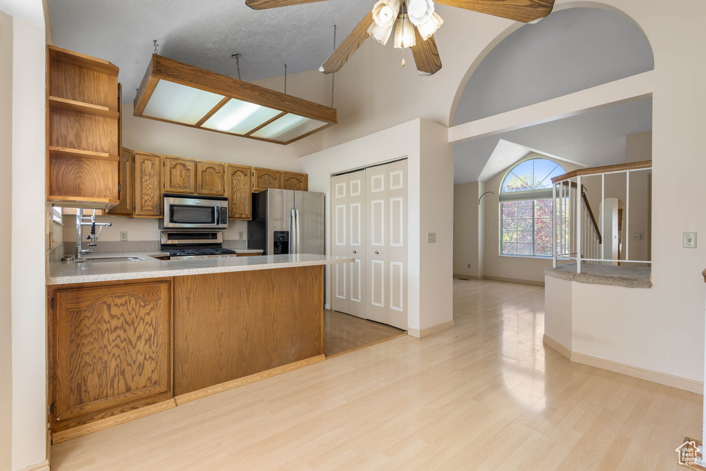 Kitchen with appliances with stainless steel finishes, a sink, light wood-style floors, a peninsula, and open shelves