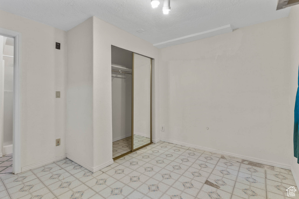 Unfurnished bedroom with light flooring, a textured ceiling, a closet, and baseboards