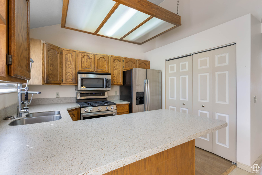 Kitchen with appliances with stainless steel finishes, a sink, light countertops, vaulted ceiling, and a peninsula