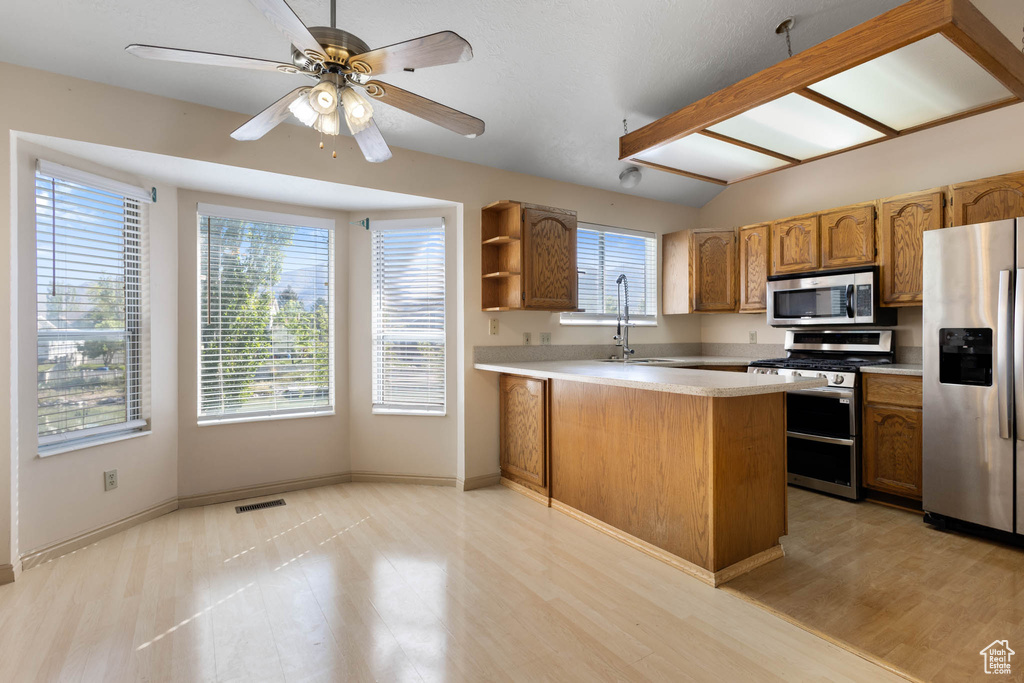 Kitchen featuring appliances with stainless steel finishes, a peninsula, open shelves, light wood-style flooring, and a ceiling fan