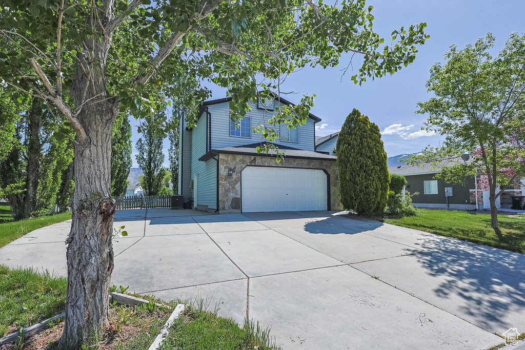 Traditional home with concrete driveway, an attached garage, stone siding, and fence