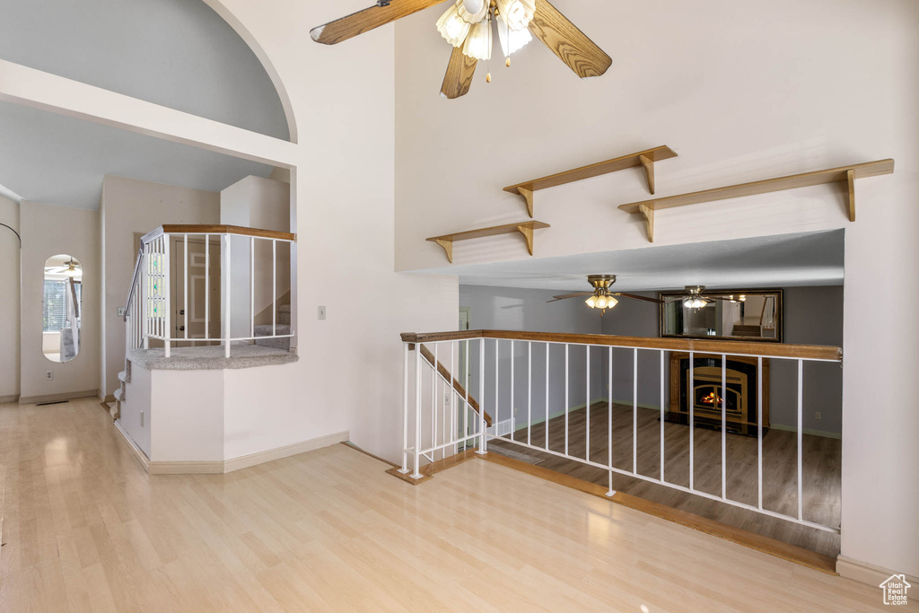 Empty room featuring ceiling fan, wood finished floors, baseboards, stairs, and a high ceiling