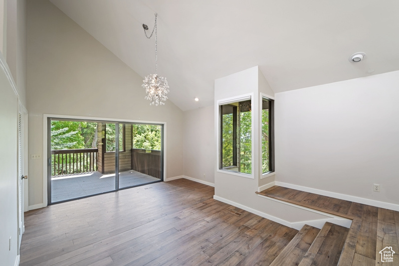 Unfurnished room featuring plenty of natural light, a chandelier, high vaulted ceiling, wood finished floors, and baseboards
