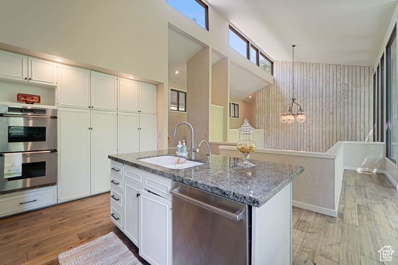 Kitchen featuring a sink, appliances with stainless steel finishes, light wood-style floors, pendant lighting, and dark stone counters