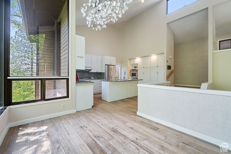 Kitchen with appliances with stainless steel finishes, a kitchen island with sink, high vaulted ceiling, a chandelier, and light wood-style flooring