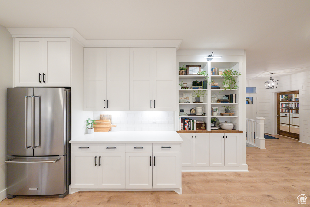 Kitchen with high end fridge, light wood-style floors, white cabinetry, light countertops, and open shelves