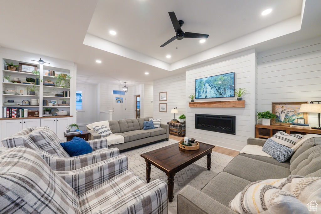 Living area featuring ceiling fan, a raised ceiling, a fireplace, recessed lighting, and wood finished floors
