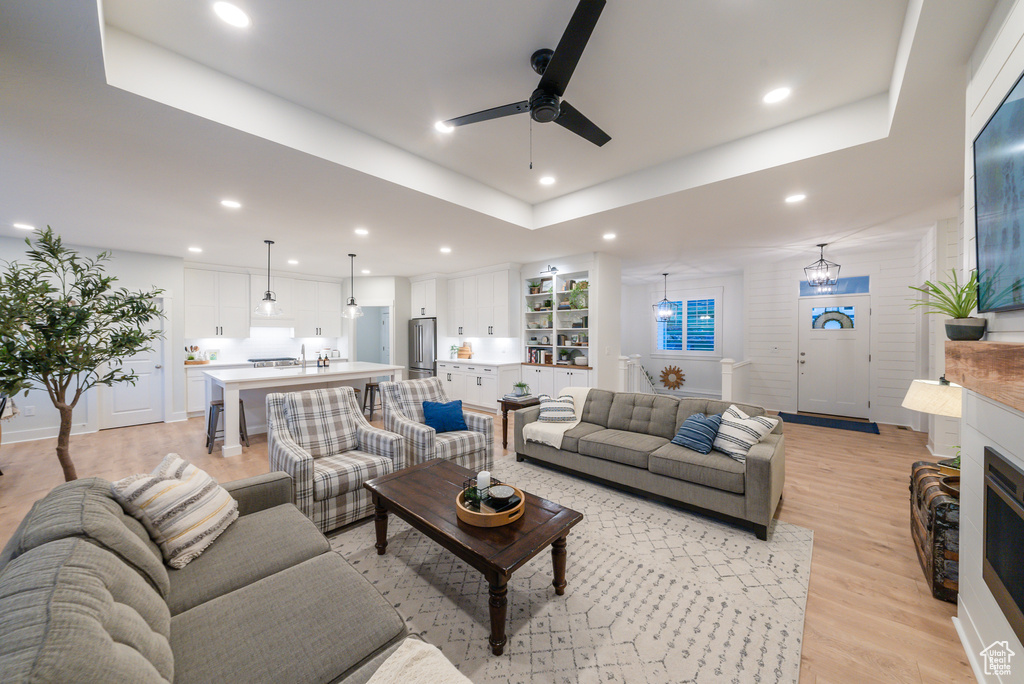 Living area featuring a ceiling fan, light wood-style floors, recessed lighting, a raised ceiling, and a fireplace