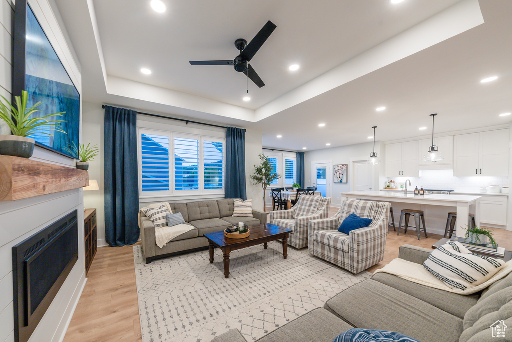 Living area featuring ceiling fan, a tray ceiling, light wood-type flooring, a fireplace, and recessed lighting
