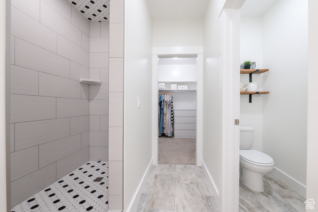 Bathroom with a tile shower, toilet, baseboards, and marble finish flooring