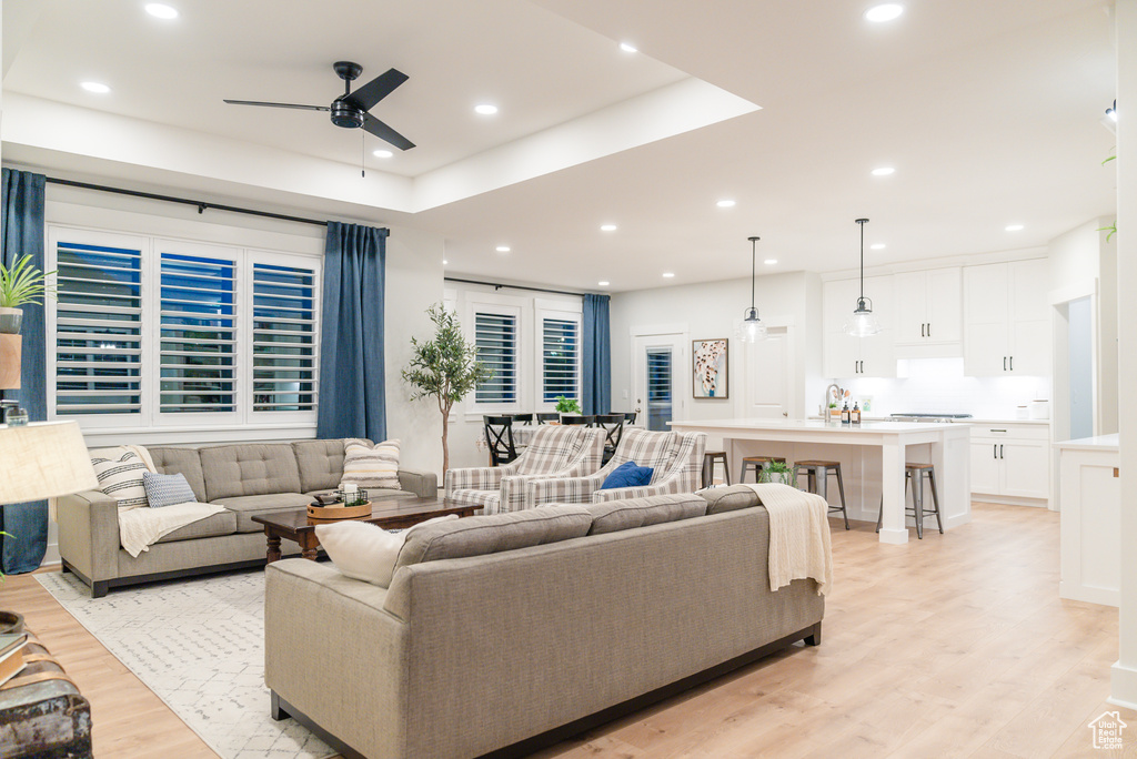 Living area with a ceiling fan, light wood finished floors, recessed lighting, and a tray ceiling