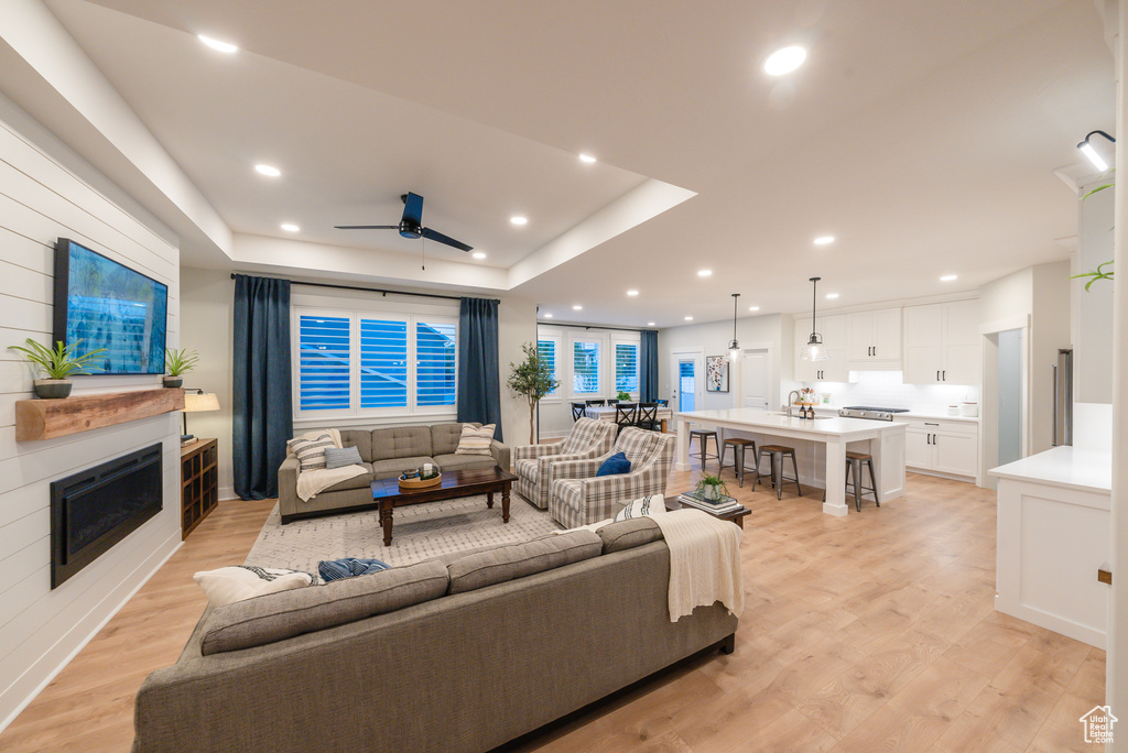 Living area with light wood-style flooring, a tray ceiling, a ceiling fan, a fireplace, and recessed lighting