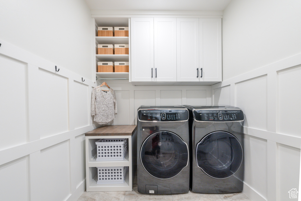 Laundry room featuring a decorative wall, washer and dryer, cabinet space, and a wainscoted wall