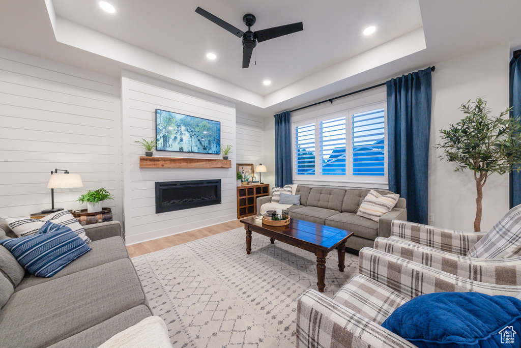 Living room featuring a tray ceiling, a ceiling fan, wood finished floors, a fireplace, and recessed lighting
