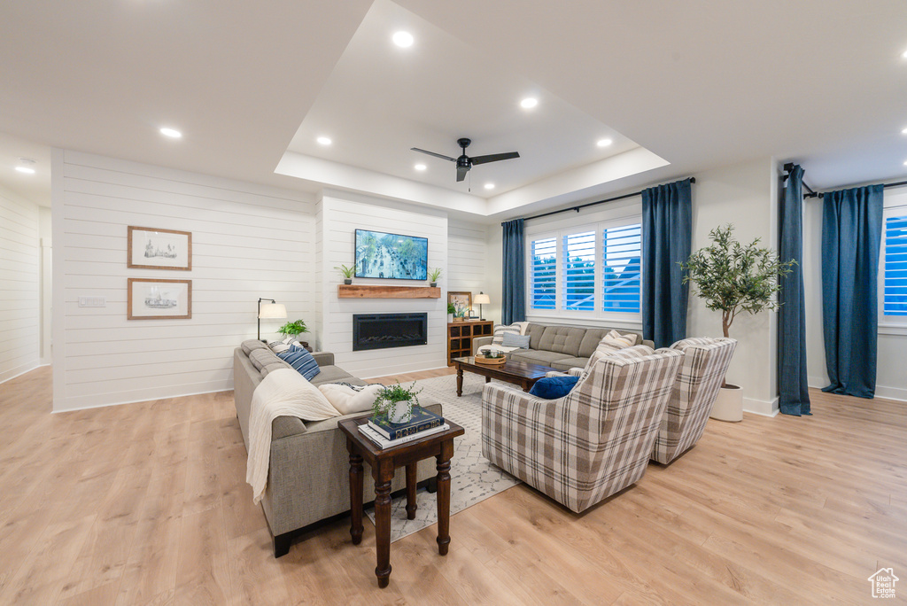 Living area featuring a ceiling fan, a raised ceiling, light wood-type flooring, a fireplace, and recessed lighting
