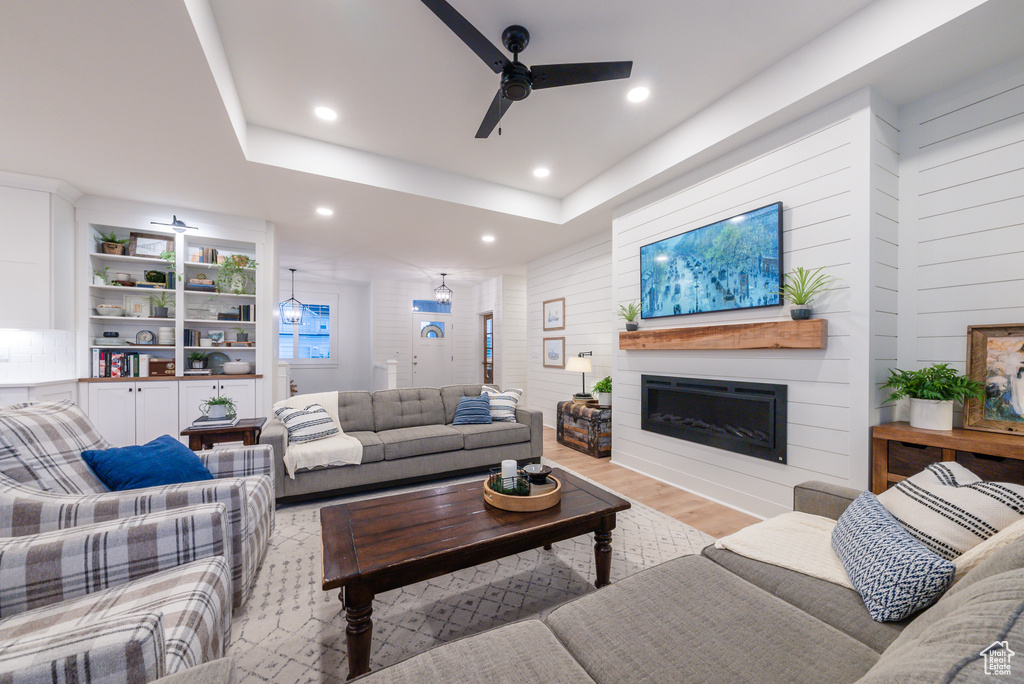 Living room with a ceiling fan, a fireplace, wood finished floors, recessed lighting, and a tray ceiling