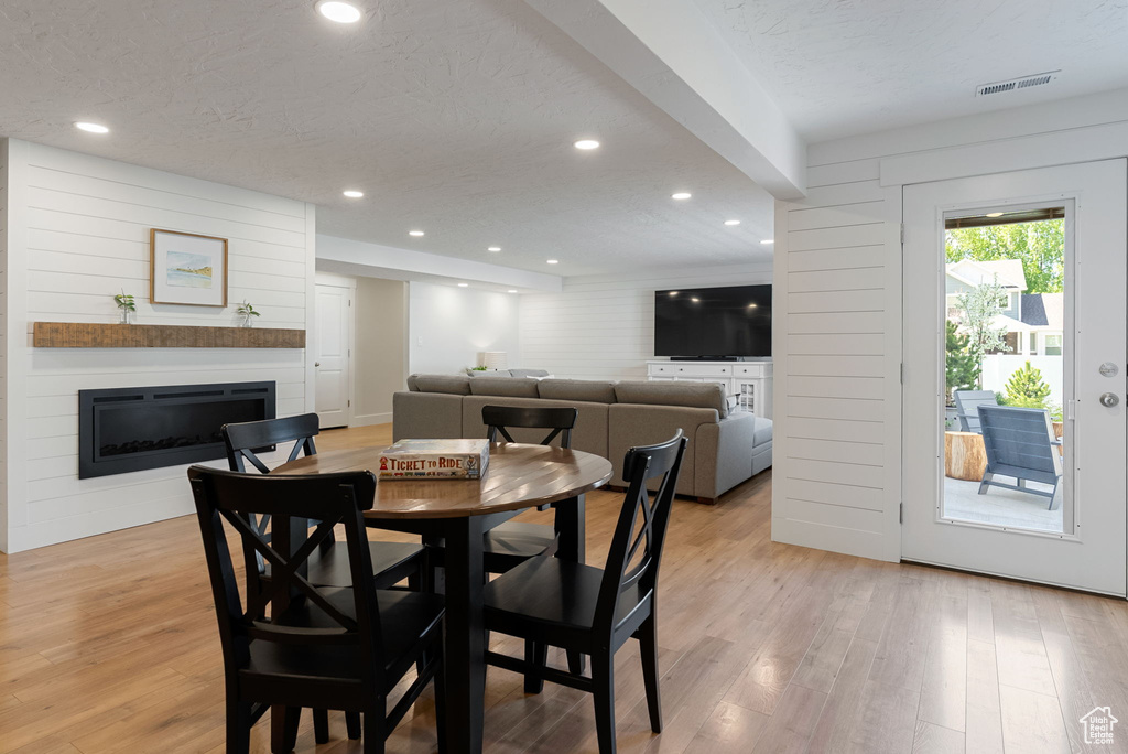 Dining space featuring light wood-type flooring, a glass covered fireplace, recessed lighting, and a textured ceiling