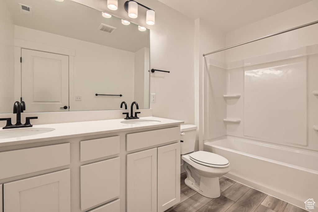 Bathroom with wood finished floors, toilet, double vanity, and  shower combination