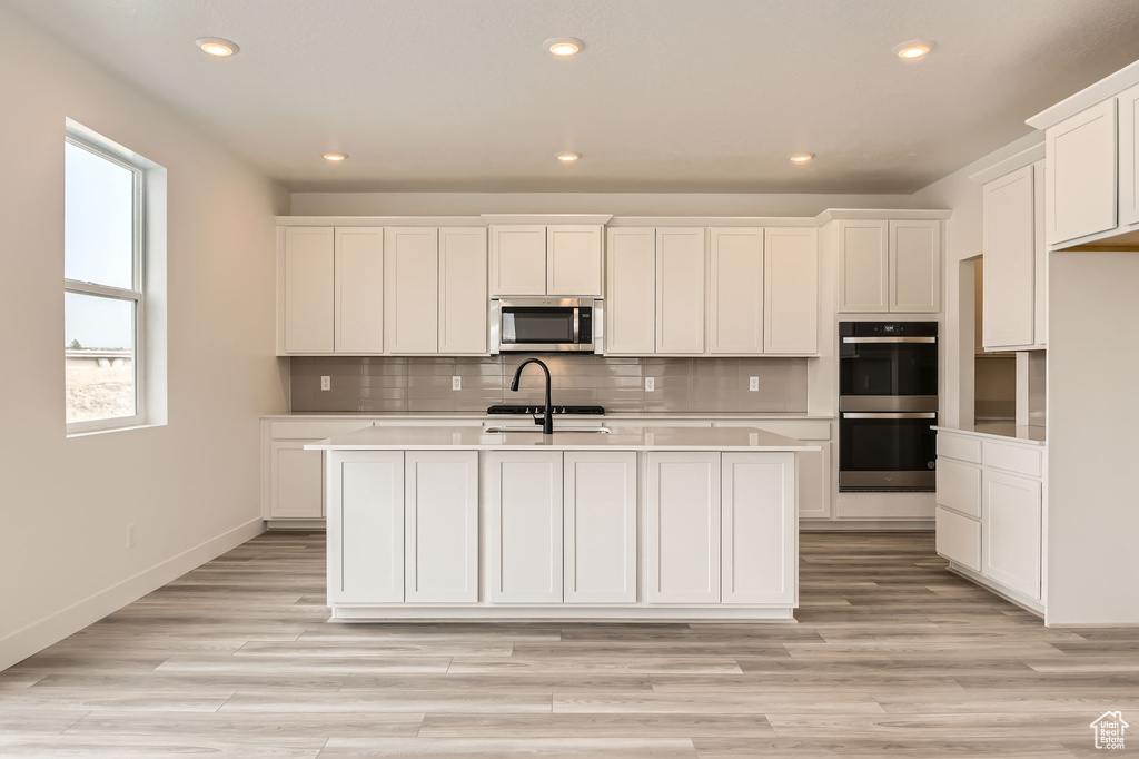 Kitchen with appliances with stainless steel finishes, recessed lighting, a center island with sink, backsplash, and light countertops