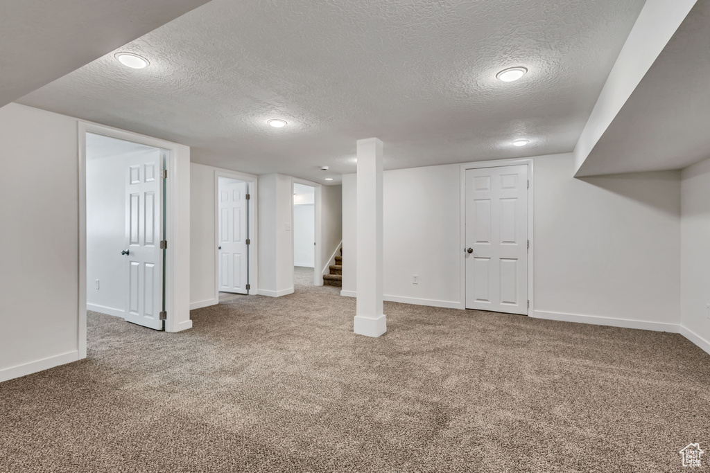 Finished basement featuring a textured ceiling, carpet, baseboards, and stairway