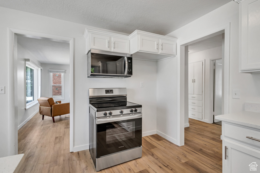 Kitchen featuring appliances with stainless steel finishes, light wood-style flooring, light countertops, and white cabinetry
