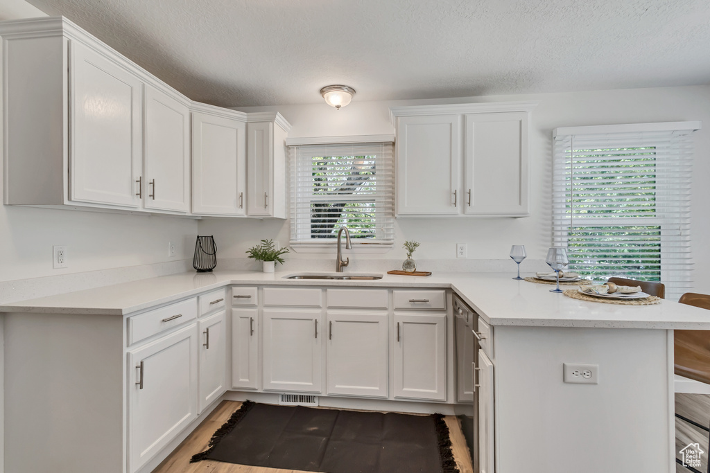 Kitchen featuring a sink, a peninsula, light countertops, white cabinets, and a textured ceiling