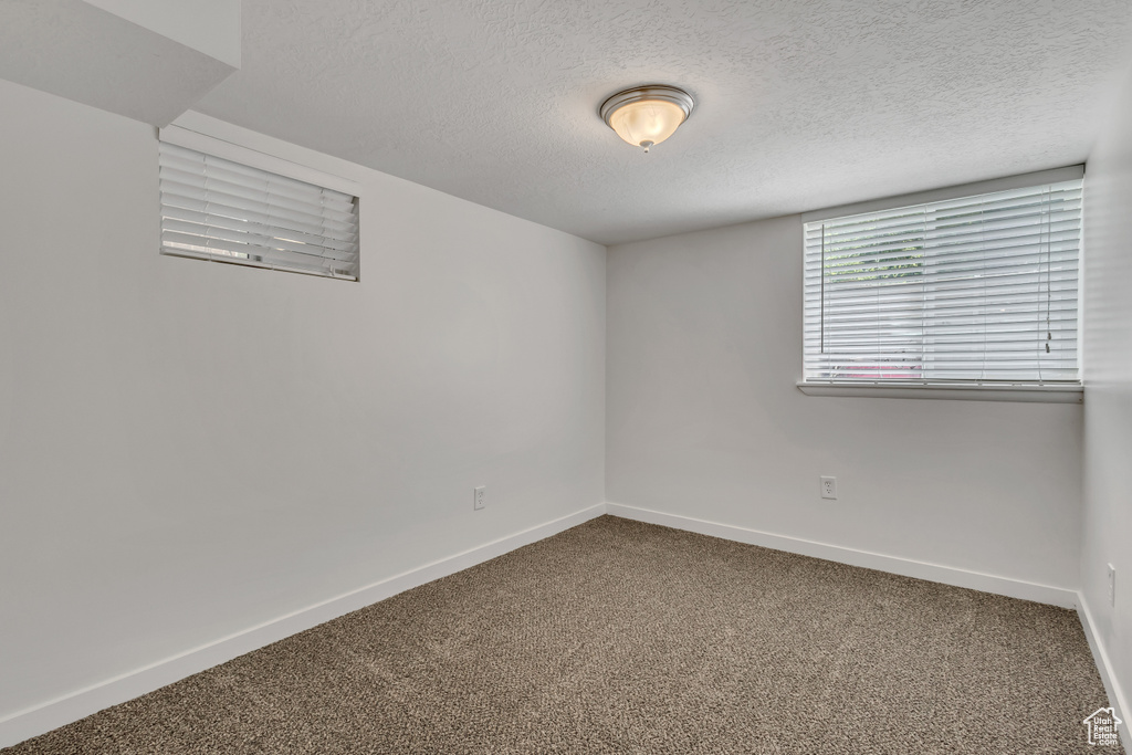 Empty room with carpet, a textured ceiling, and baseboards