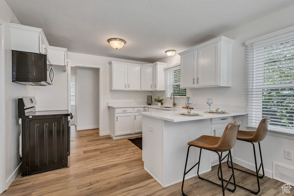Kitchen with stainless steel microwave, electric range oven, a sink, a peninsula, and white cabinets