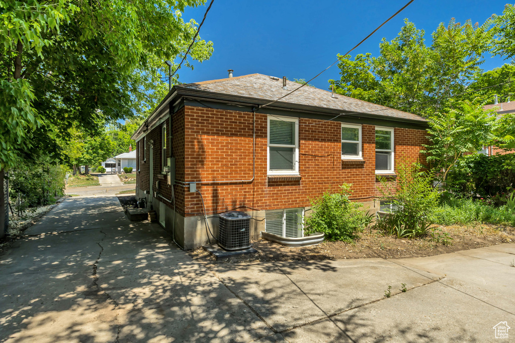 View of property exterior with brick siding, driveway, and a shingled roof