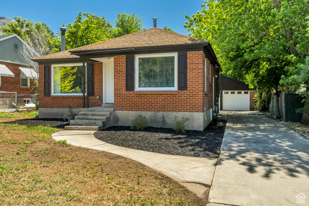 Bungalow with driveway, brick siding, entry steps, an outbuilding, and a detached garage