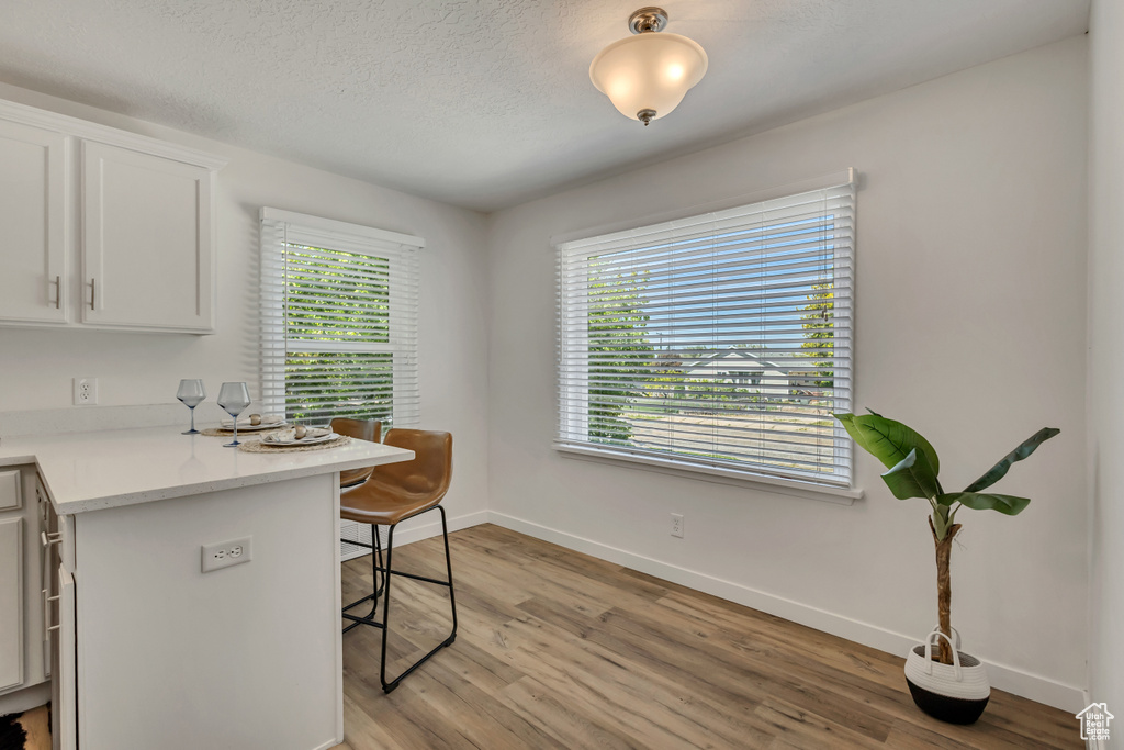 Kitchen featuring a breakfast bar, light wood-type flooring, baseboards, white cabinetry, and a textured ceiling