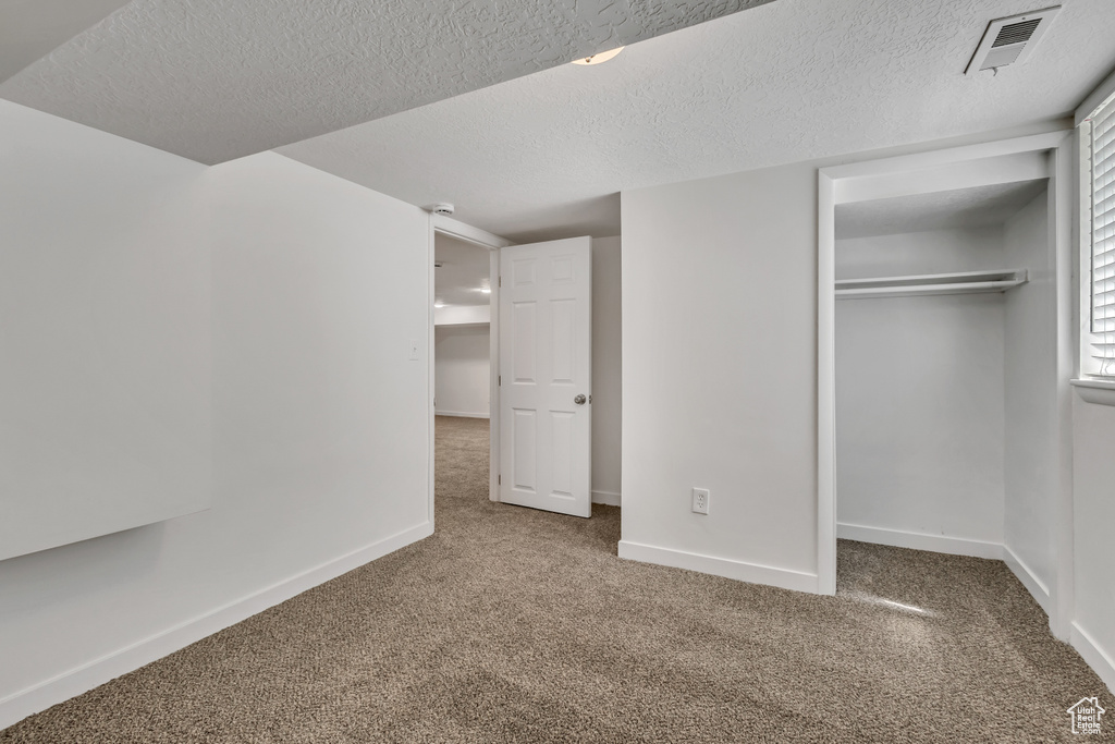 Unfurnished bedroom featuring carpet, a closet, a textured ceiling, and baseboards