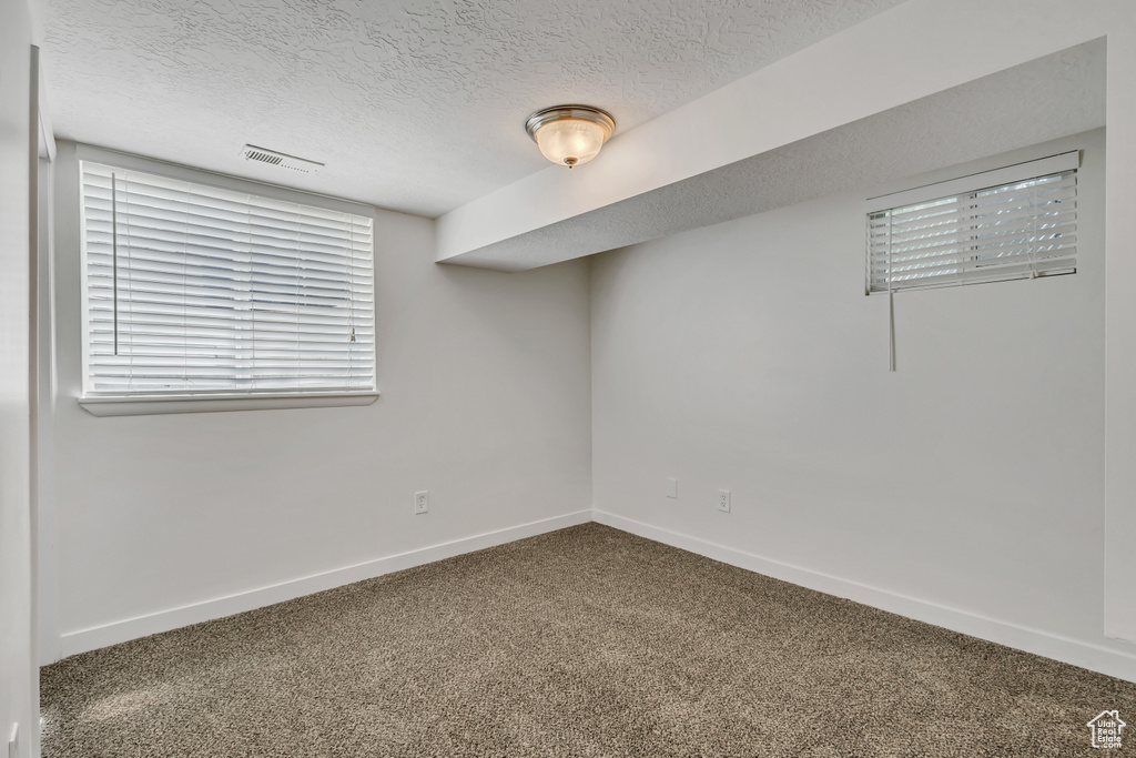 Carpeted spare room with a textured ceiling and baseboards